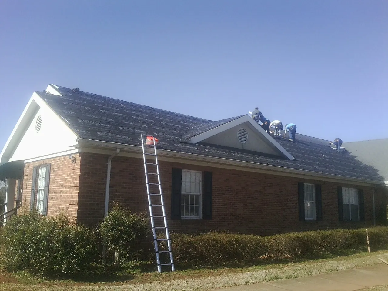 Crew tearing shingles off a brick ranch roof with a ladder set — Emergency Roof Repair work by our crew in Onamia