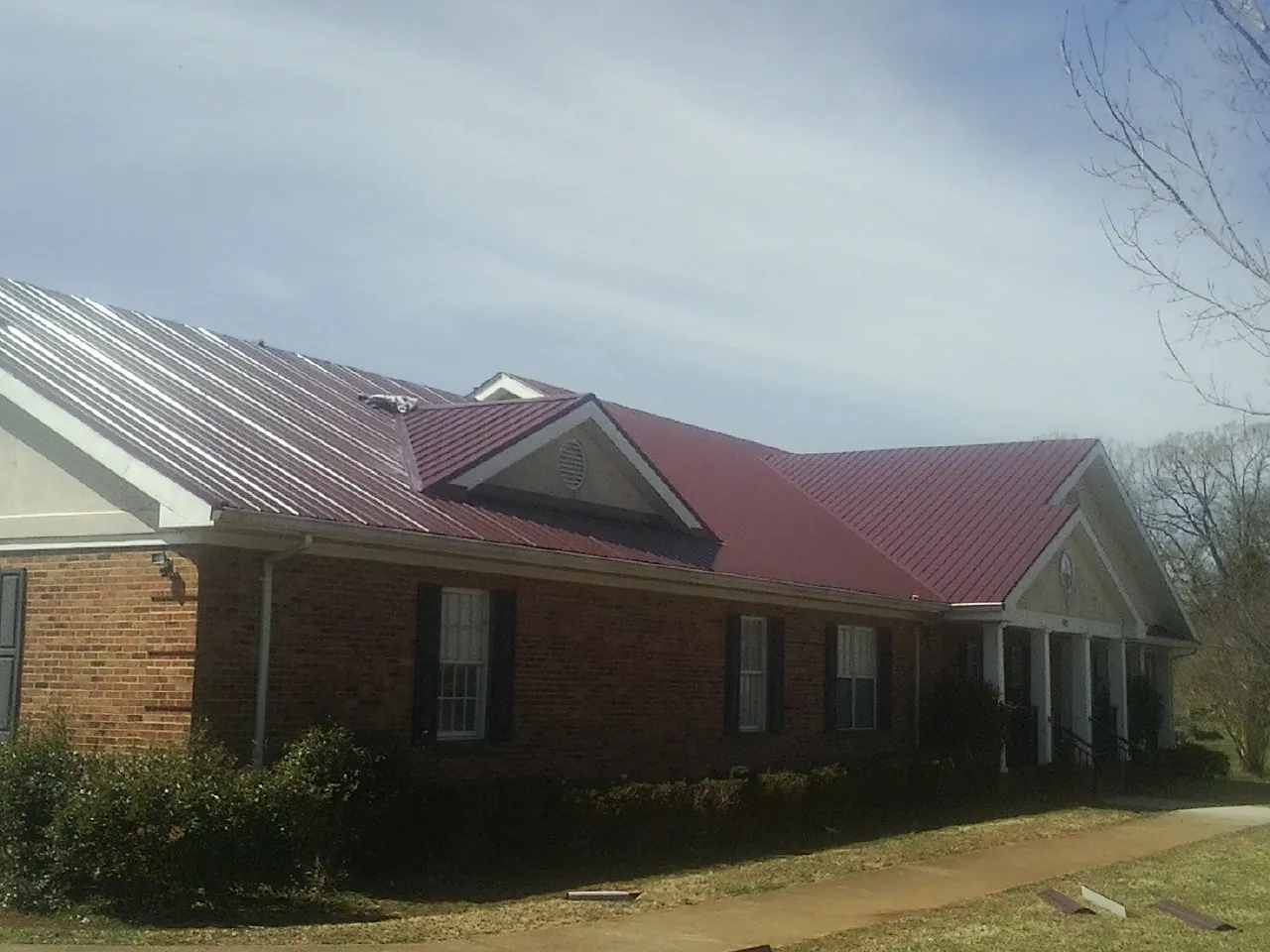 Red metal roof with gabled entries on a long brick building, from a Hail Damage Roof Repair job in Onamia