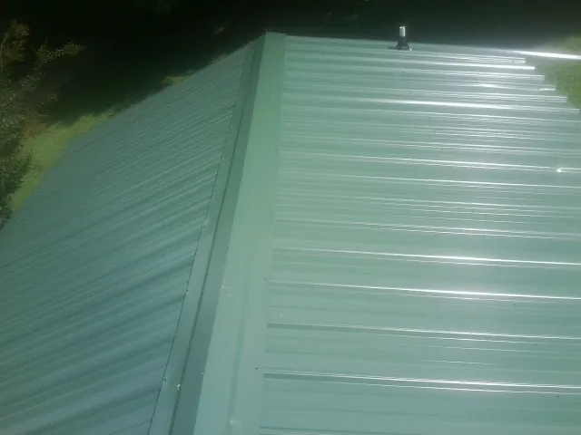 New green metal panels meeting at the ridge of a roof — Flat Roof Repair work by our crew in Onamia