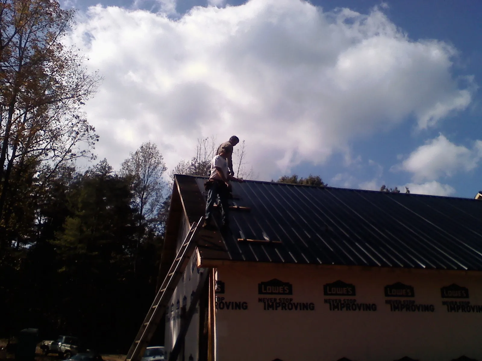 Roofer fastening dark metal panels high against a cloudy sky, from a Roof Inspection job in Onamia
