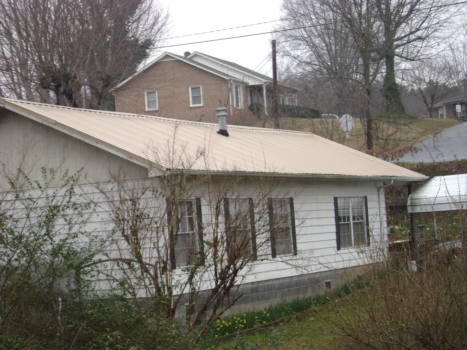 Tan metal roof on a white sided house set into a hillside — Commercial Roofing by Roofing Brothers in Onamia