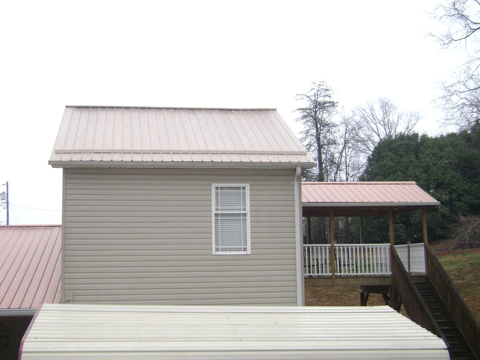 Tan metal roofs on a two story addition and attached porch, from a Roof Replacement job in Onamia